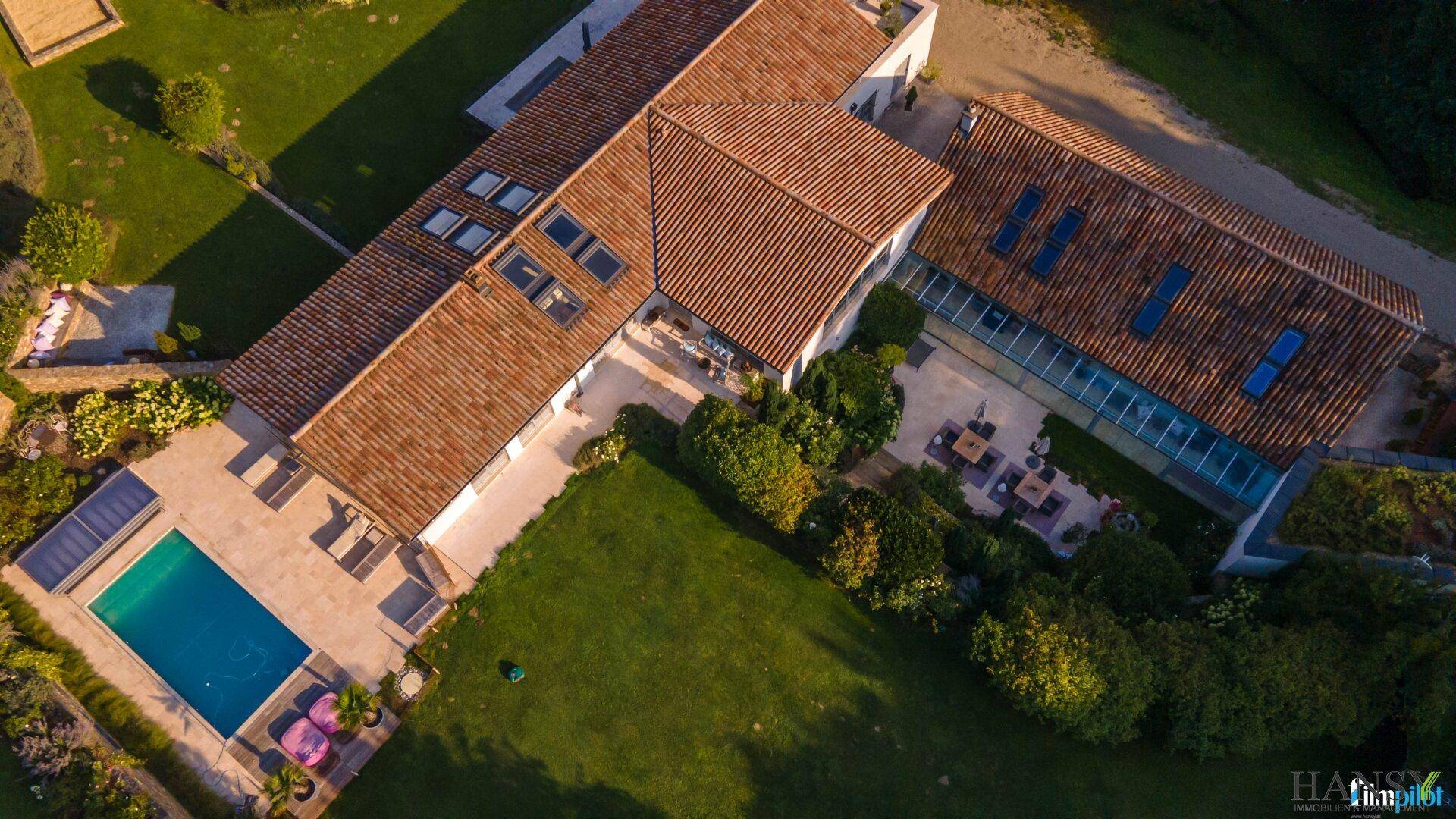 Luftaufnahme des Anwesens mit Pool, weitläufiger Terrasse und einem verglasten Wintergartenbereich.
