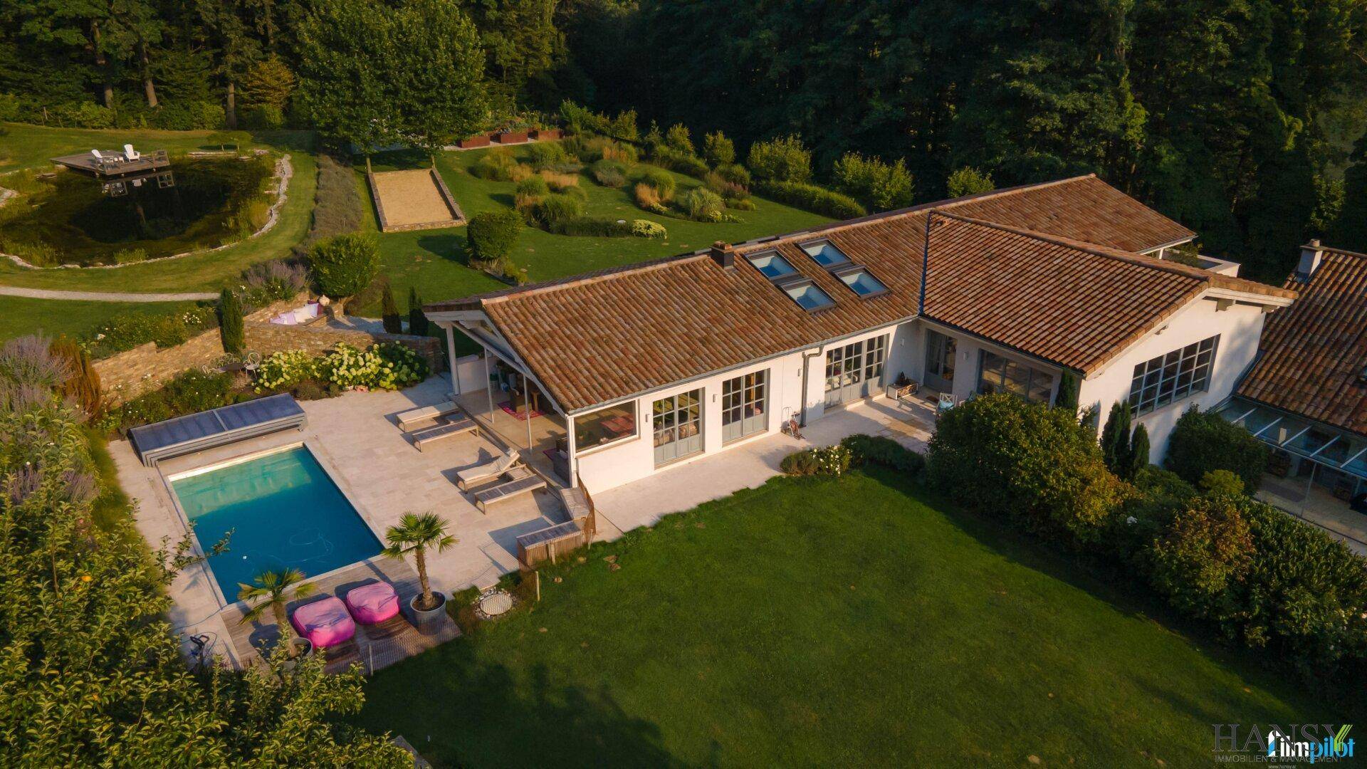 Elegantes Landhaus mit großem Poolbereich und weitläufigem Garten, umgeben von üppigem Grün.