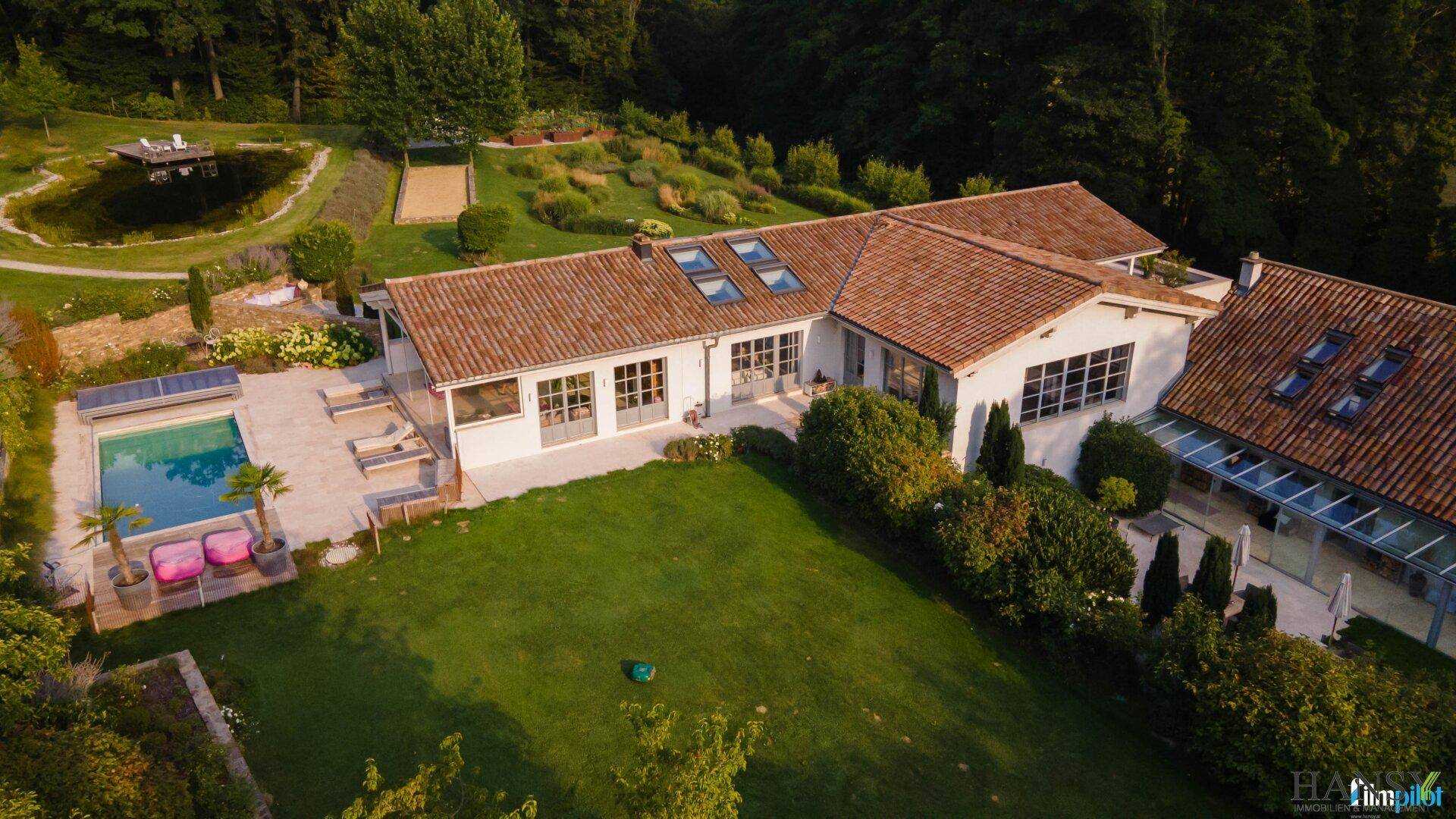 Weitläufiger Gartenbereich mit Teich und Blick auf das elegante Landhaus umgeben von viel Grün.