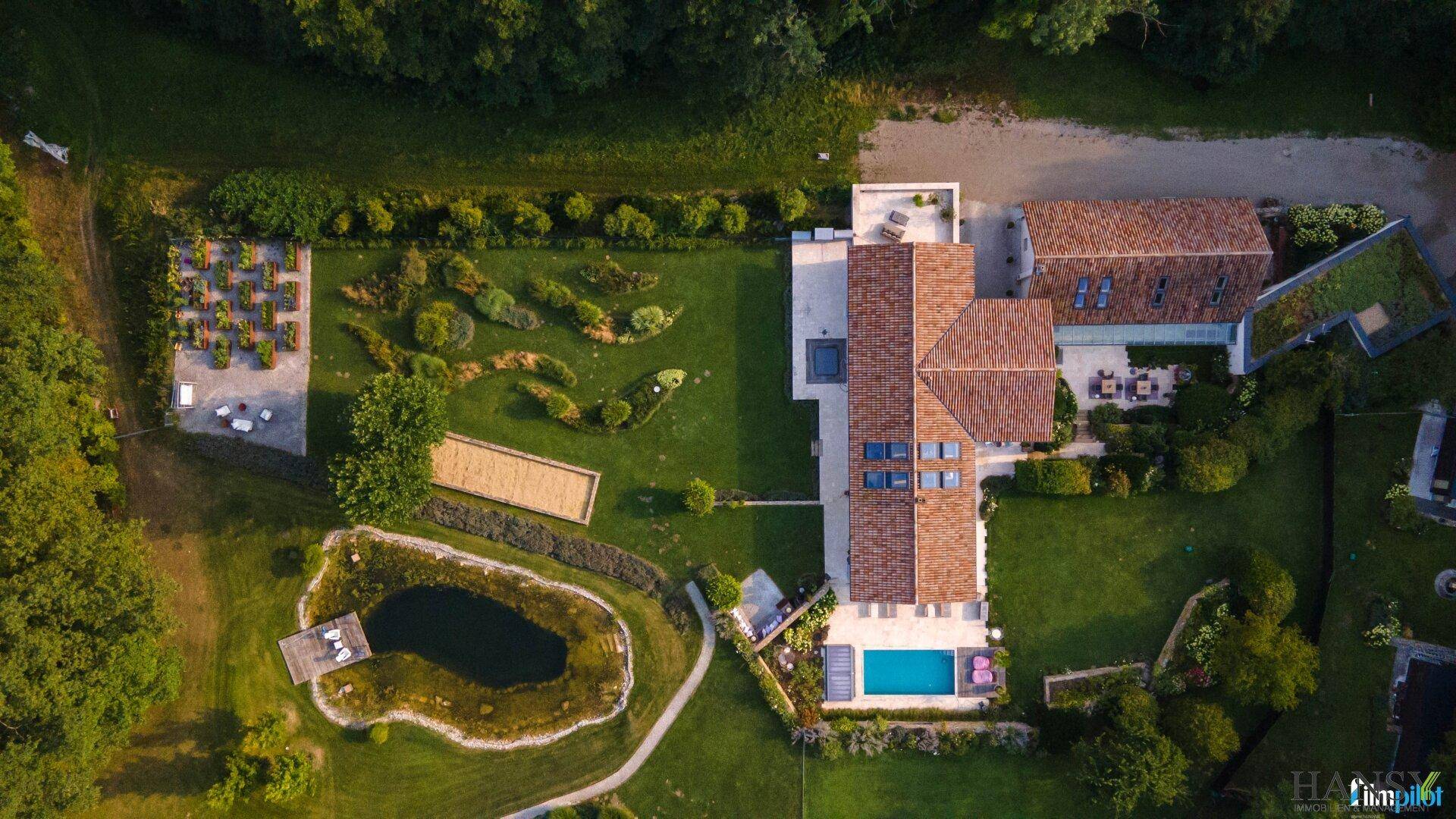 Gesamtansicht des weitläufigen Anwesens von oben mit Haus, Pool, Teich und verschiedenen Gartenbereichen.