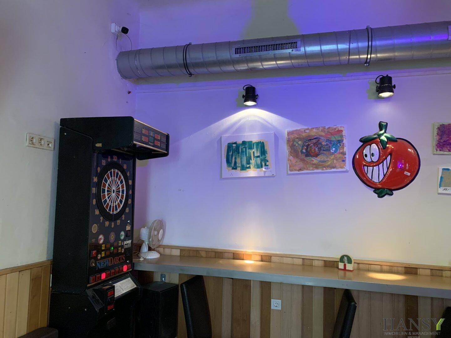 Dartbereich mit langer Theke, Wandkunst und indirekter Beleuchtung.