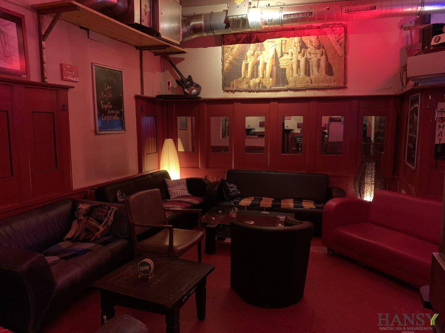 Gemütlicher Lounge-Bereich mit Ledersofas, Sesseln und Holztischen auf rotem Boden.