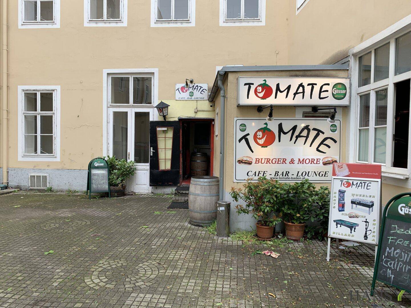 Außenansicht des Eingangs zum "TOMATE" Café-Bar-Lounge mit gepflastertem Vorplatz.