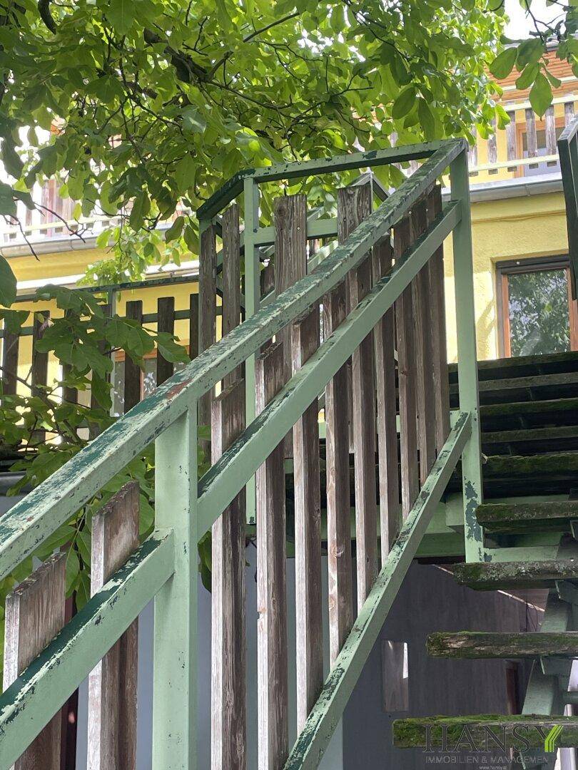 Nahaufnahme eines verwitterten Holzgeländers mit grünen Metallstreben einer Außentreppe.