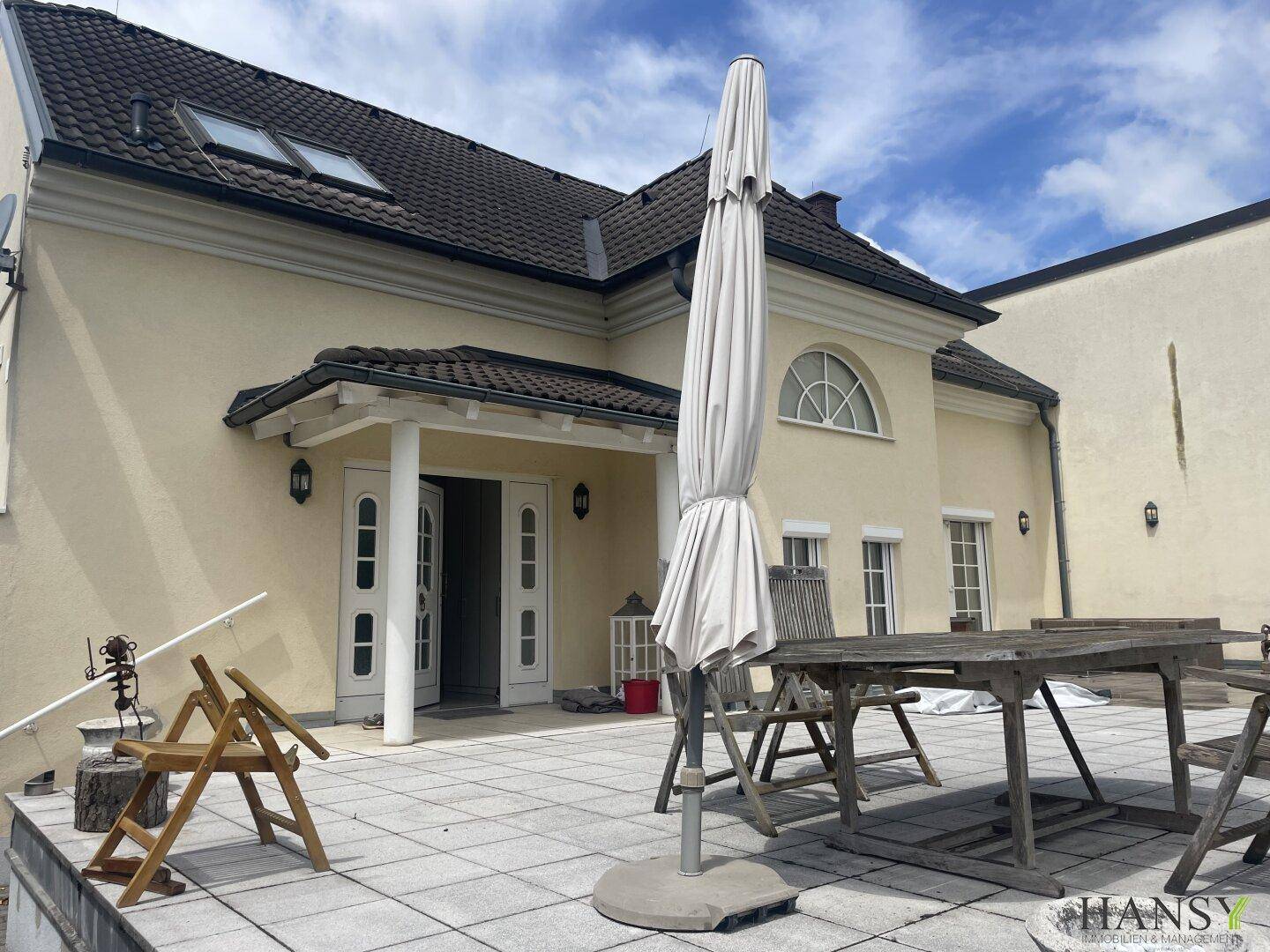 Geräumige Terrasse mit Holztisch, Stühlen und Sonnenschirm, ideal für entspannte Stunden im Freien.