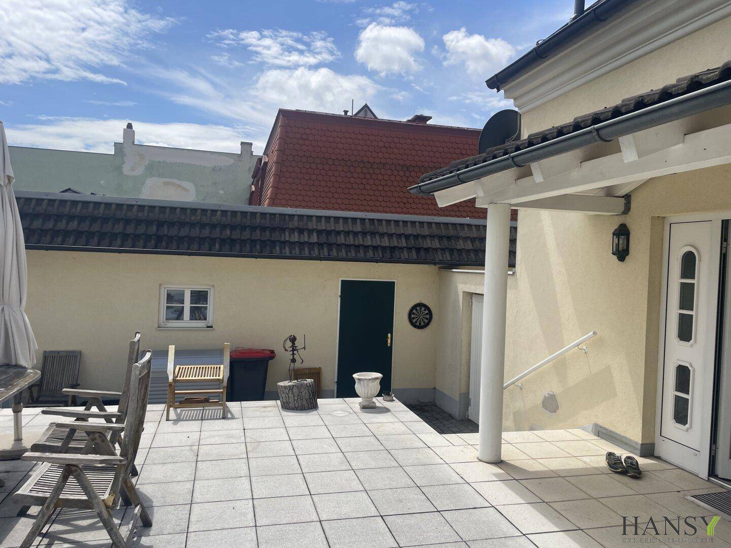 Teil der Terrasse mit gepflastertem Boden, einem Dartboard an der Wand und Blick auf den Garten.