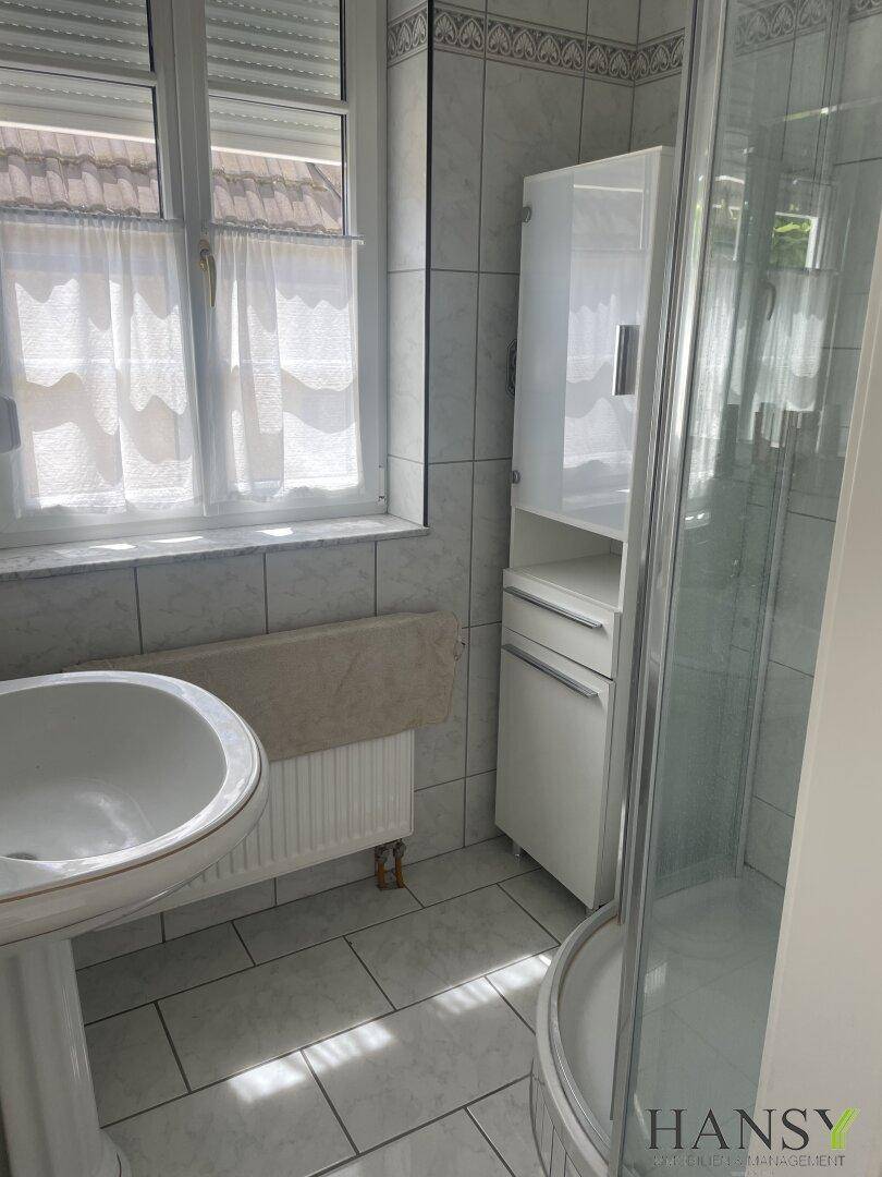 Badezimmer mit Dusche, Standwaschbecken und Fenster mit Rollläden.