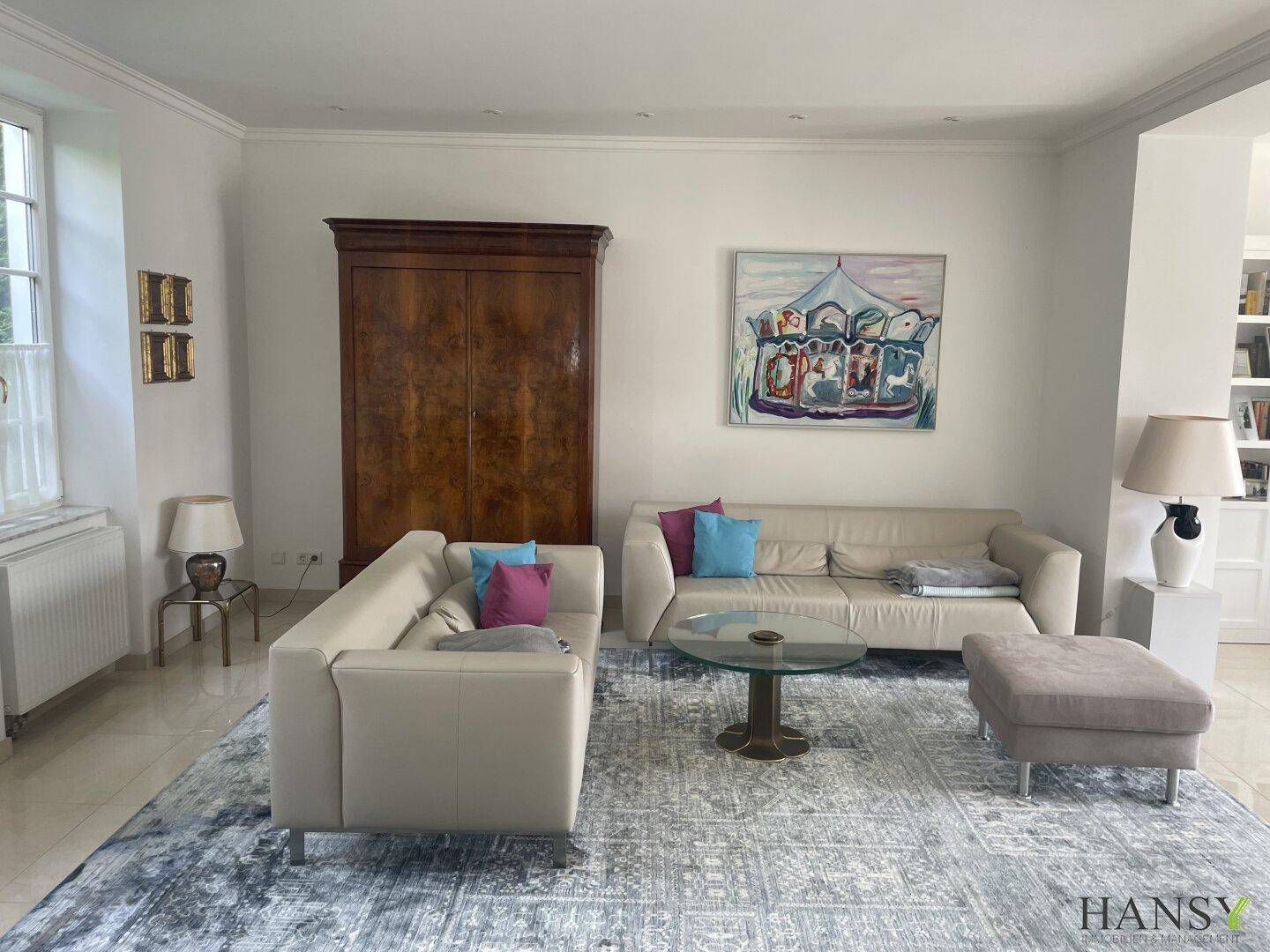 Helles Wohnzimmer mit bequemen Sofas, einem eleganten Holzschrank und Kunstwerken an den Wänden.