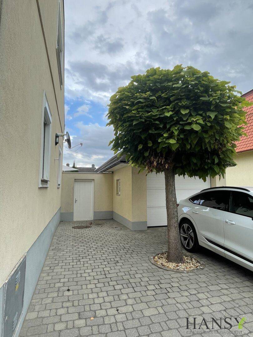Gepflasterte Einfahrt mit Baum und Garage neben dem Haus.