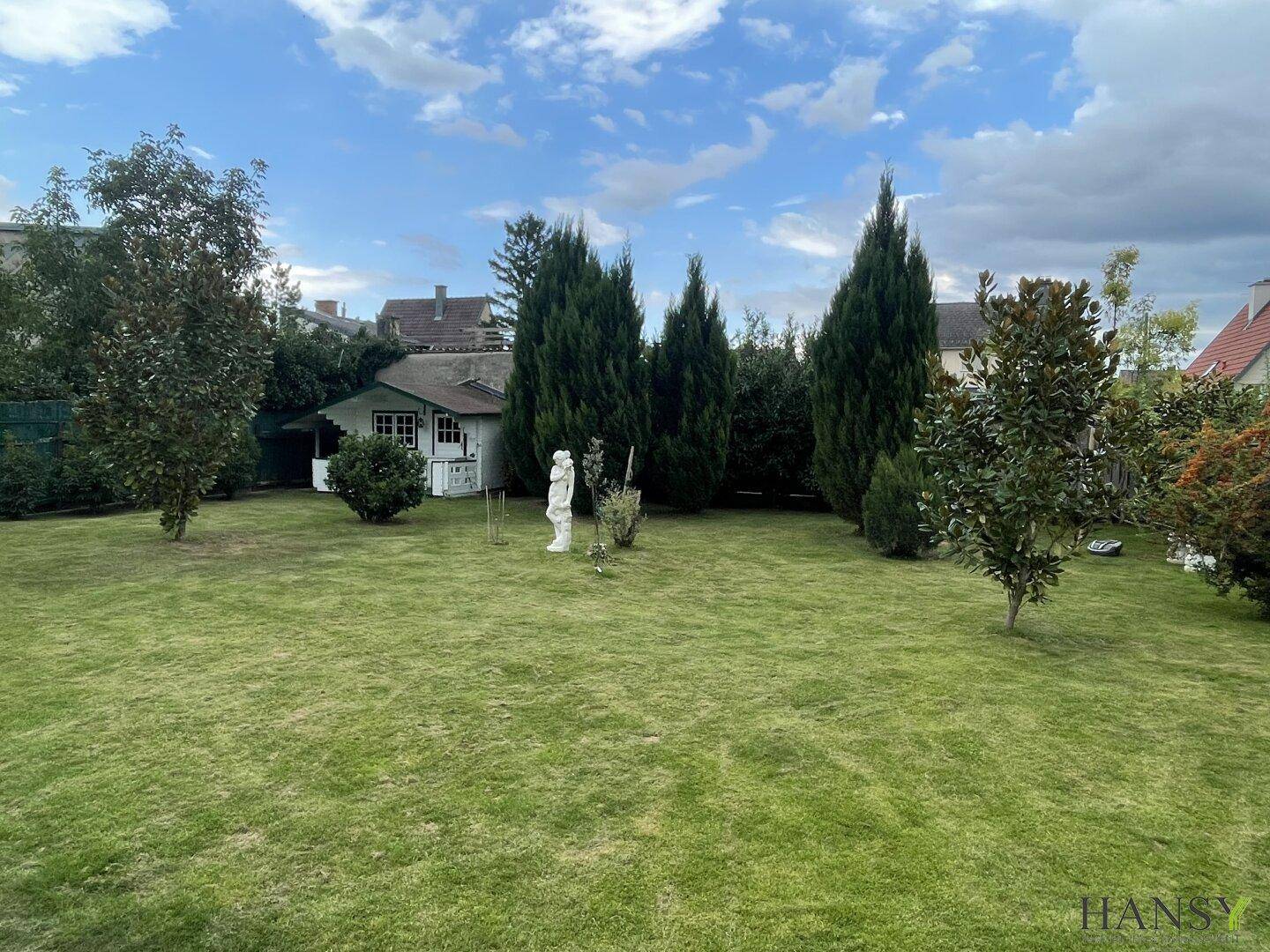 Großer Garten mit gepflegtem Rasen, hohen Bäumen und einem charmanten weißen Gartenhaus.