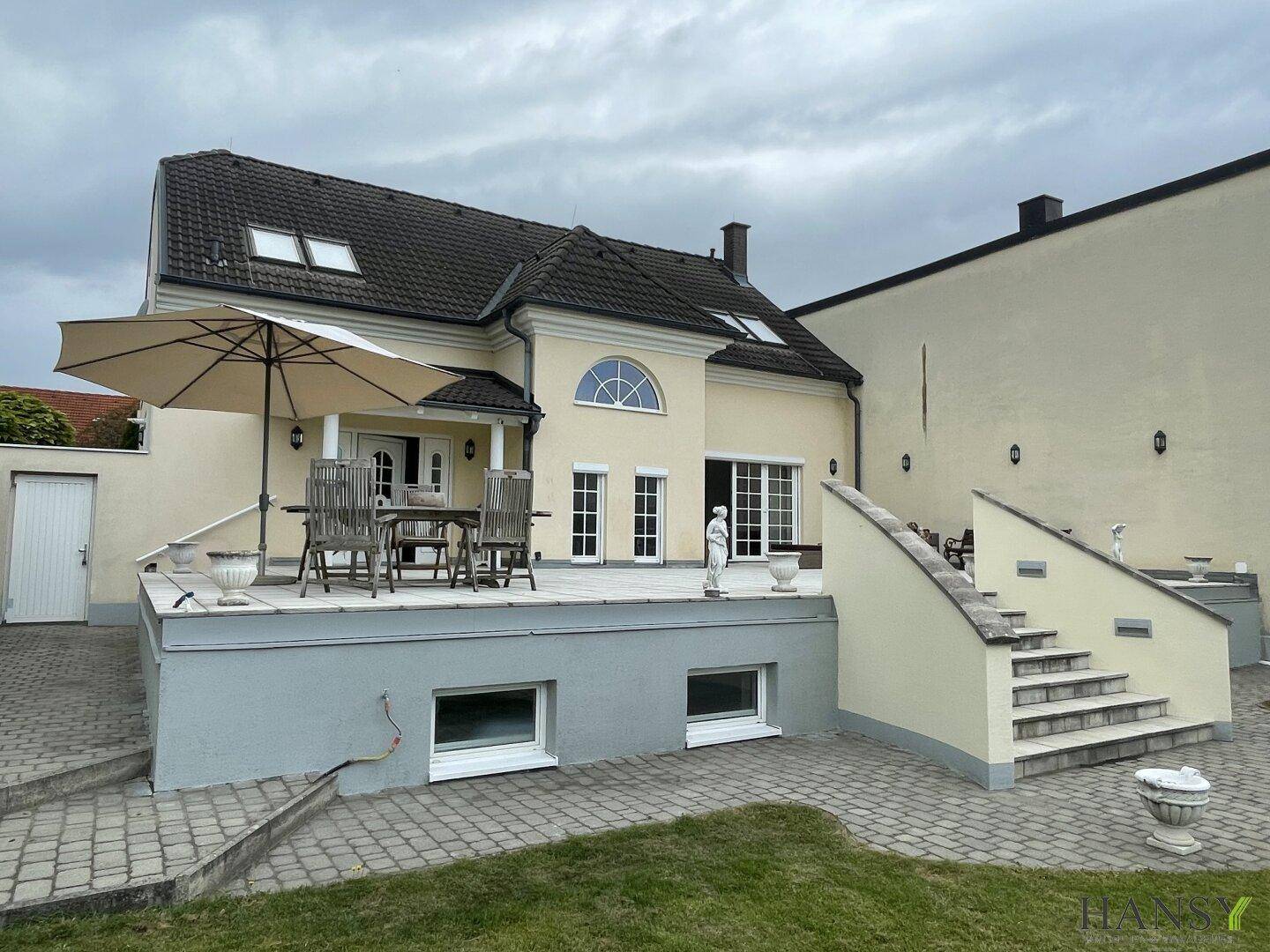 Ansicht des Hauses mit großer Terrasse, Treppe zum Garten und gepflegter Außenanlage.