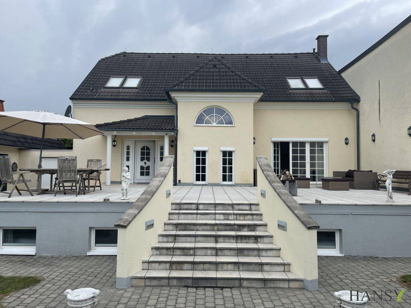Rückansicht des Hauses mit großer Terrasse, Sitzgelegenheiten und Treppe zum Garten.
