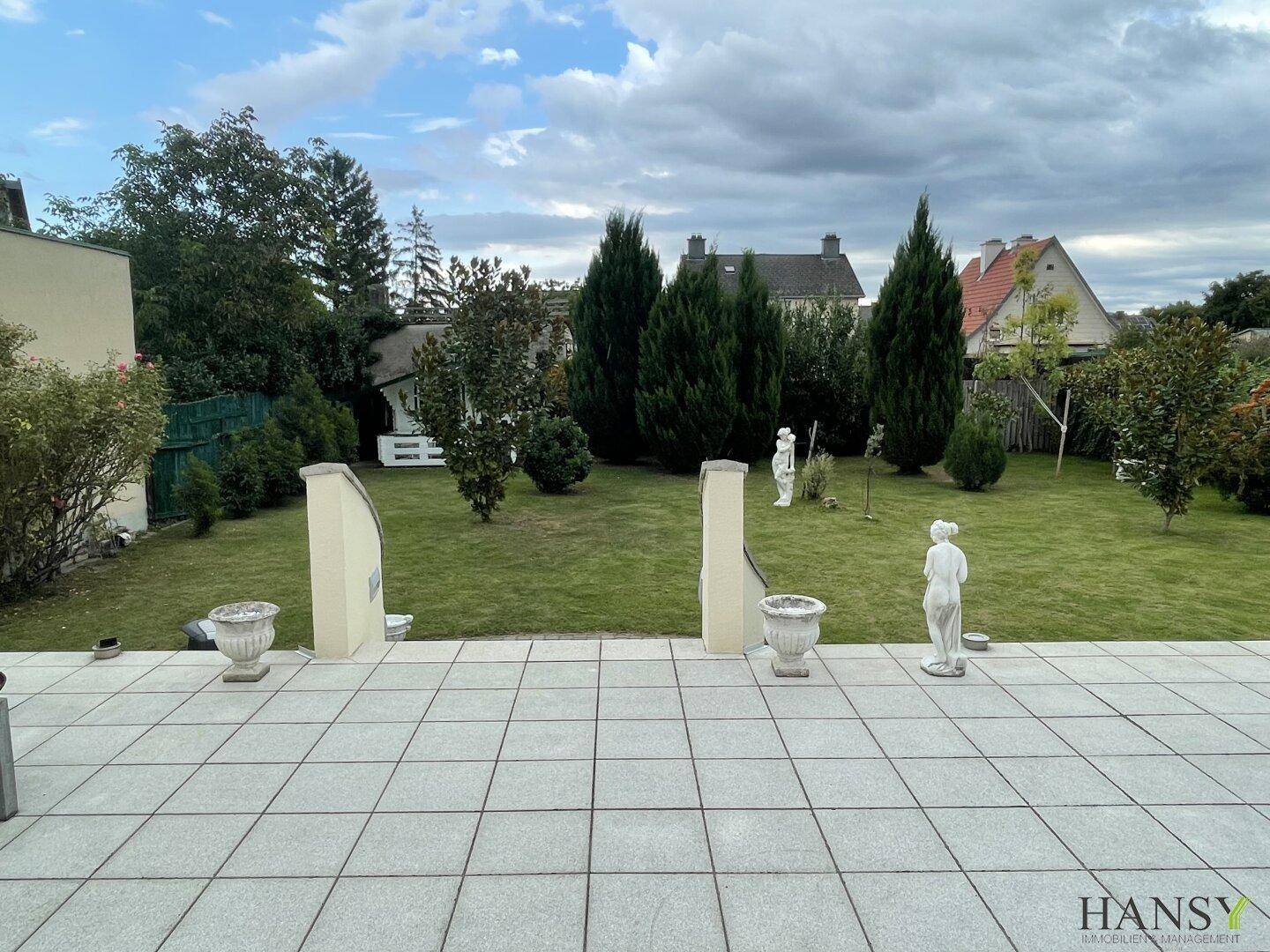 Weitläufiger Garten mit gepflegtem Rasen, Bäumen und Blick auf die umliegenden Häuser.