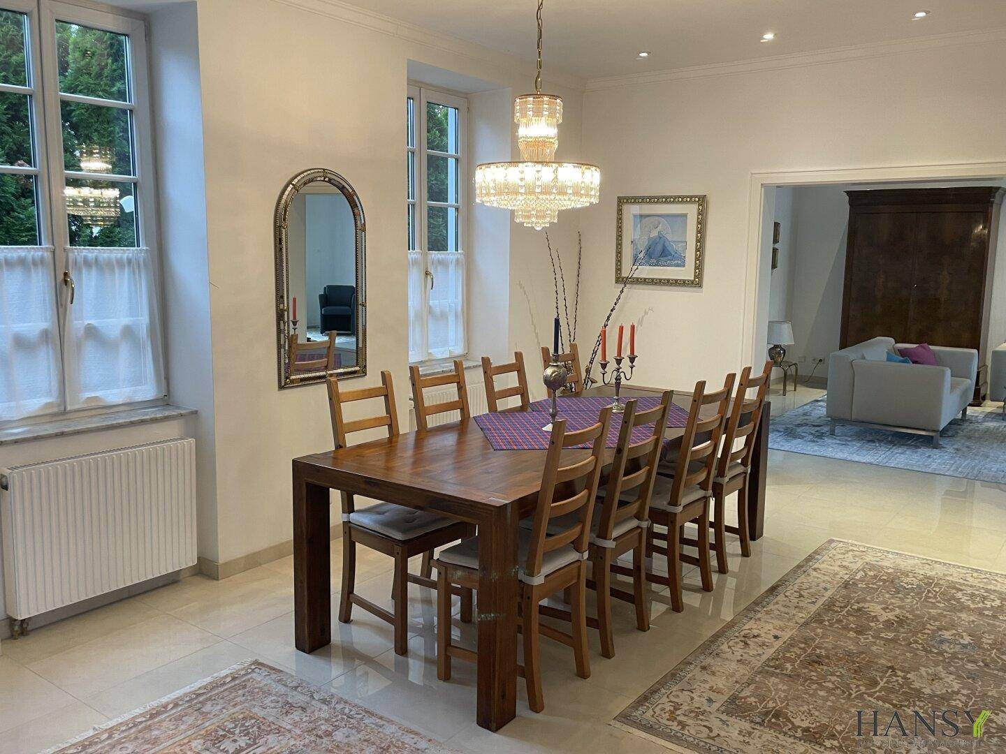 Heller Essbereich mit großem Holztisch, stilvollem Kronleuchter und Fenstern mit Blick nach draußen.