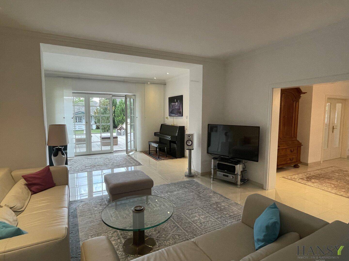 Gemütliches Wohnzimmer mit Sofas, Fernseher und Zugang zur Terrasse durch große Glastüren.