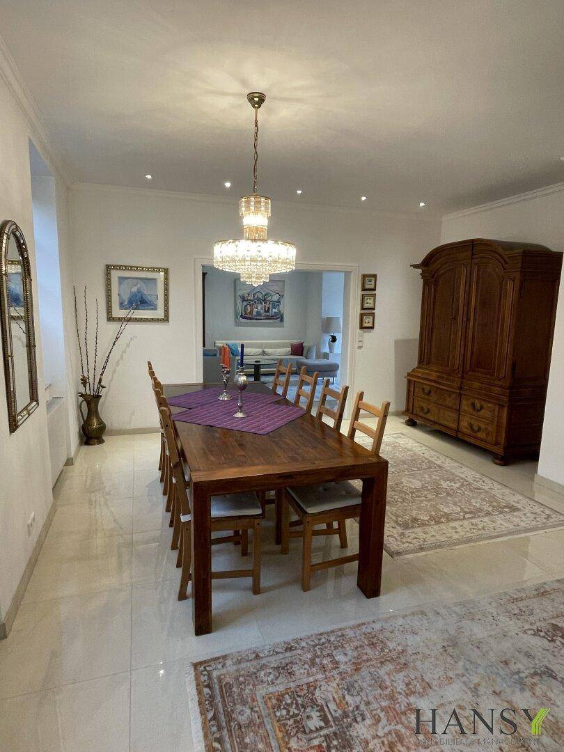 Eleganter Essbereich mit großem Holztisch, Kronleuchter und Blick in das angrenzende Wohnzimmer.