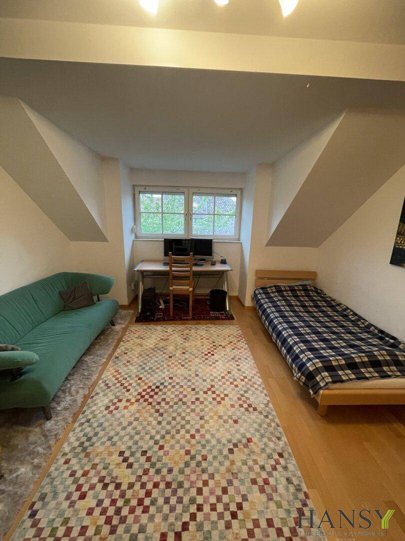 Helles Schlafzimmer mit Einzelbett, Sofa und Schreibtisch unter den Dachschrägen.