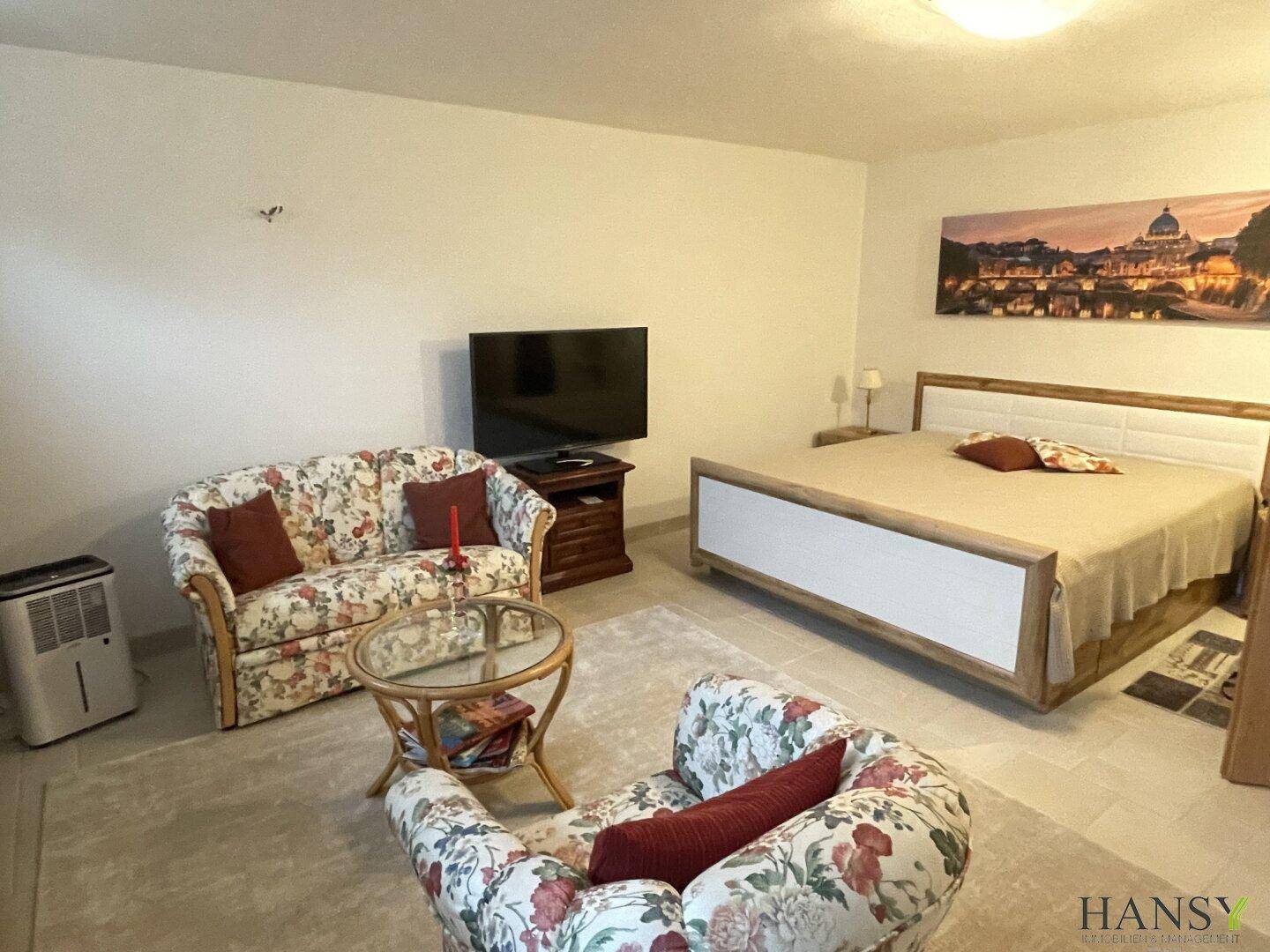 Schlafzimmer im Untergeschoss mit floralem Sofa, Bett und Fernseher.