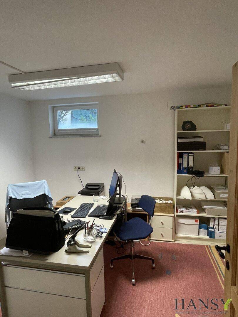 Büro im Untergeschoss mit Schreibtisch, Regal und kleinem Fenster.