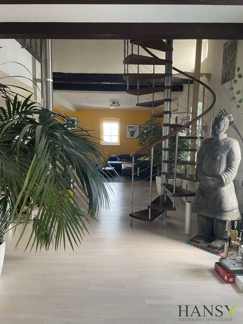 Heller Wohnbereich mit eleganter Wendeltreppe, Holzbalken und dekorativer Statue.
