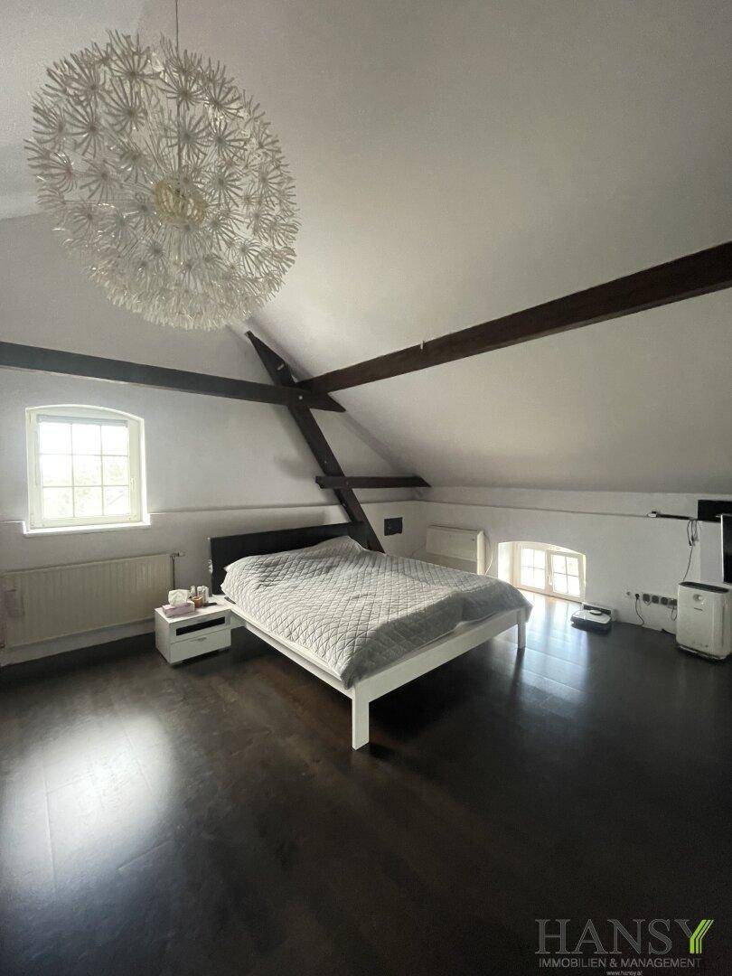 Schlafzimmer im Dachgeschoss mit dunklem Holzboden, sichtbaren Balken und Dachschräge.