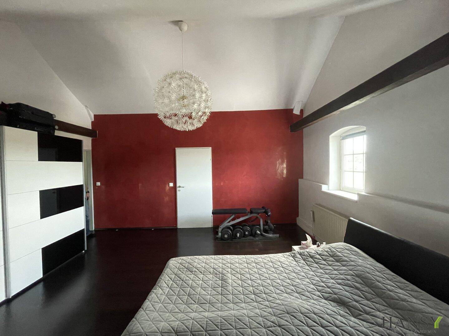Geräumiges Schlafzimmer mit roter Akzentwand, großem Kleiderschrank und Dachschräge.