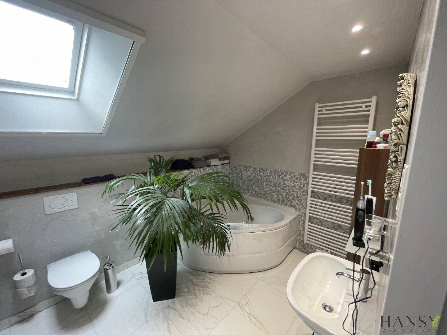 Modernes Badezimmer im Dachgeschoss mit Eckbadewanne, WC, Waschbecken und Dachfenster.