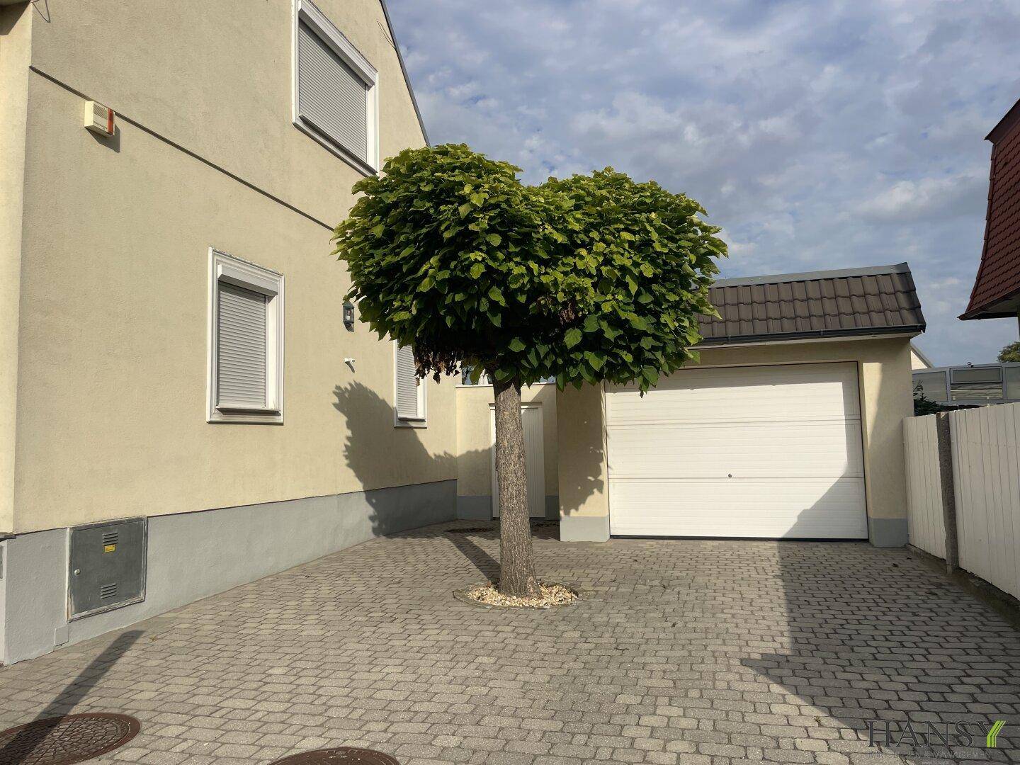 Ansicht der gepflasterten Einfahrt mit Garage und Hausfassade unter blauem Himmel.