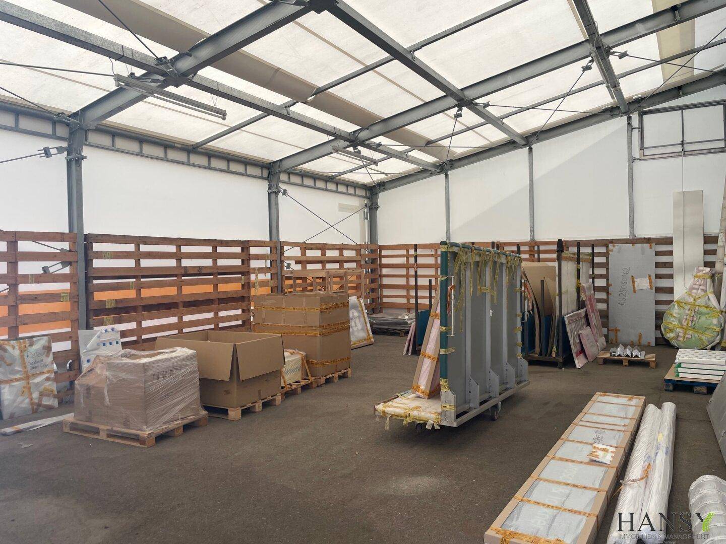 Offener Lagerbereich unter einer Zeltkonstruktion mit Holzpaletten und gelagerten Materialien, gut belüftet.
