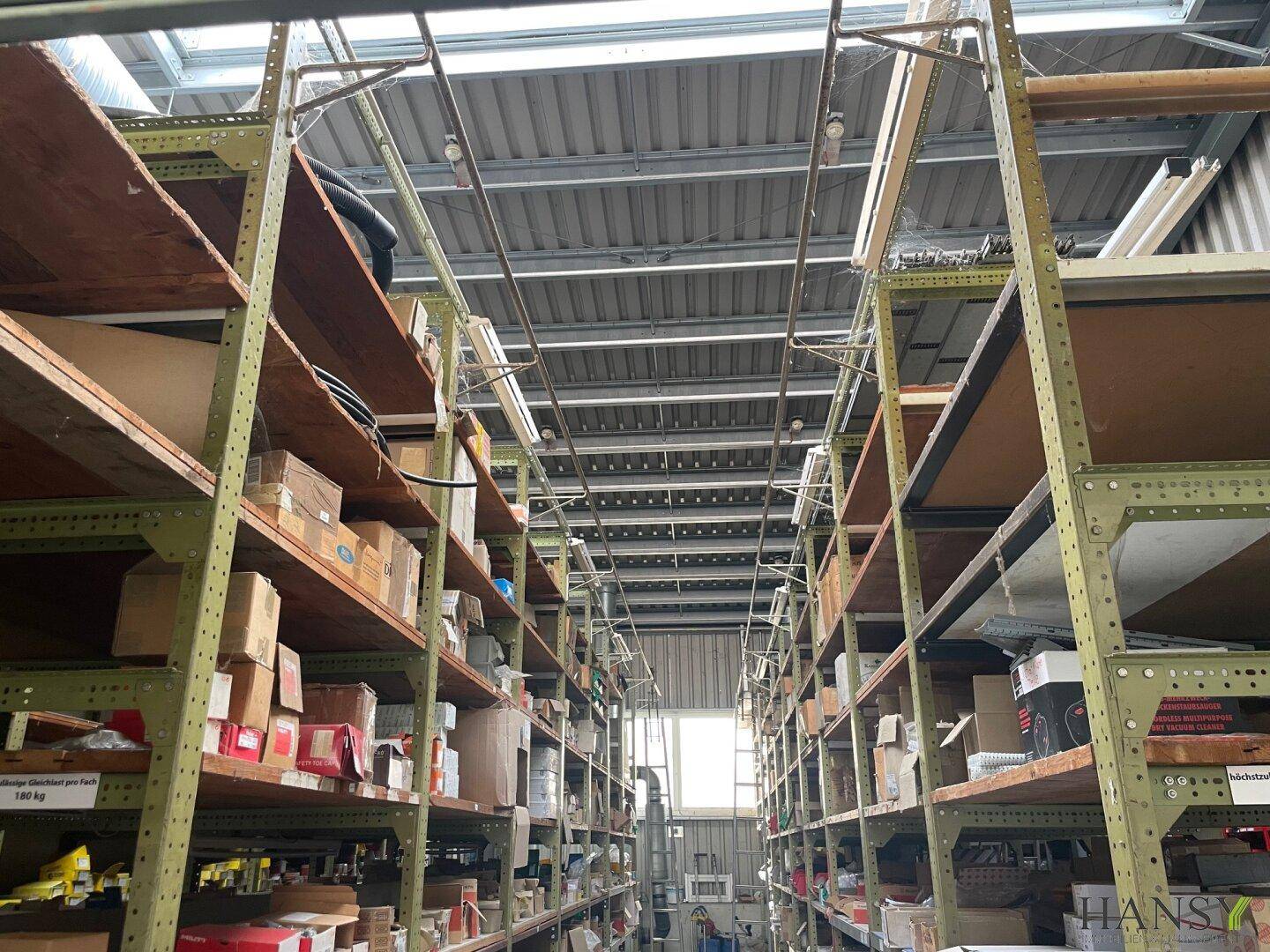 Langer Gang in einem Lagerraum mit hohen Regalen voller Kartons und einem Fenster am Ende für Tageslicht.