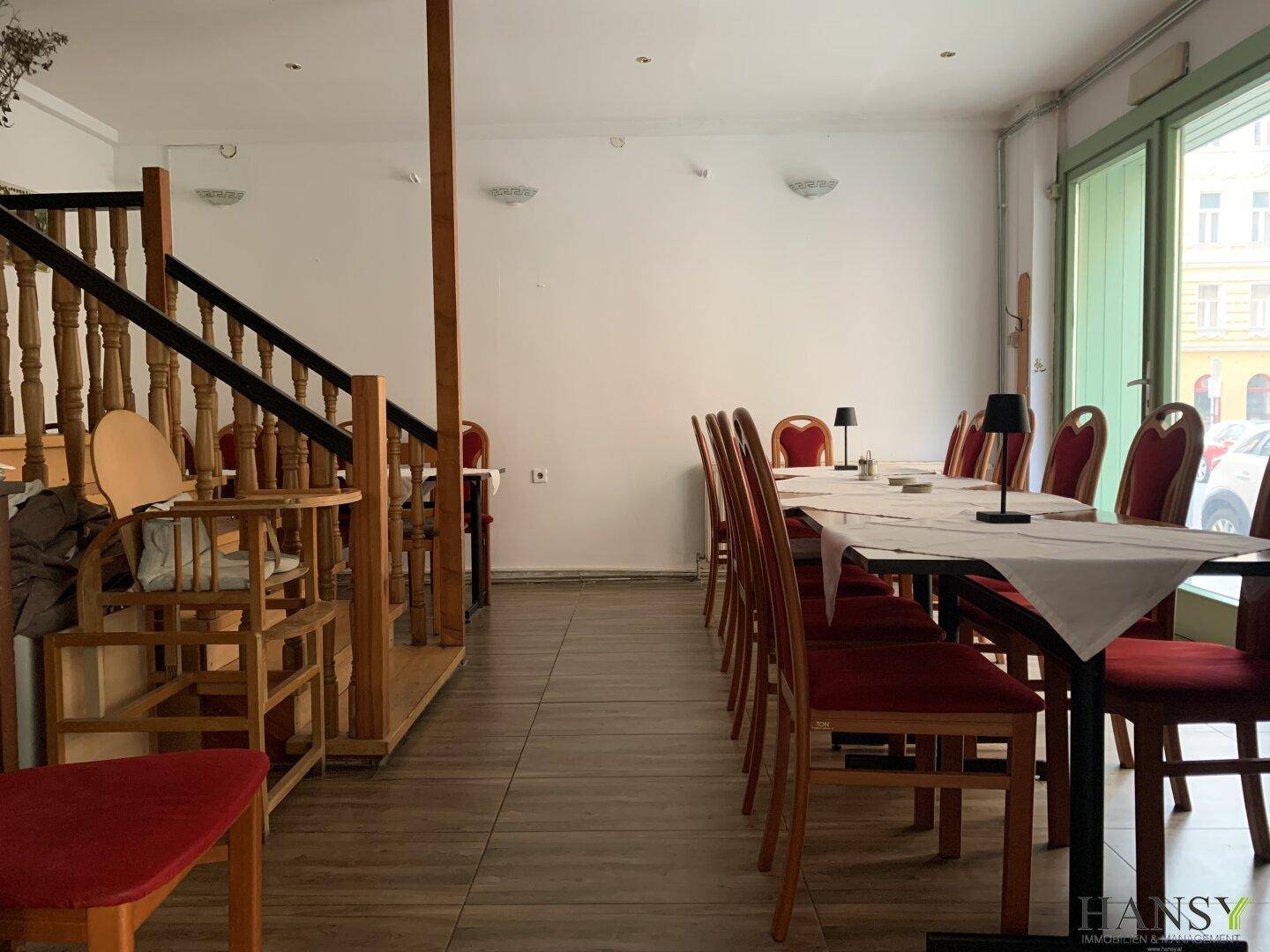 Essbereich mit Holzboden, roten Stühlen und einer Holztreppe, die in eine obere Etage führt.