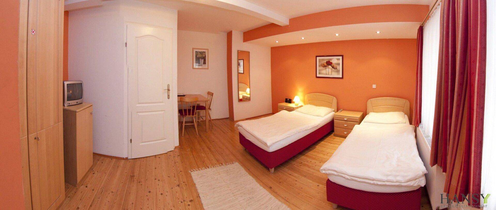 Farbenfrohes Schlafzimmer mit zwei Einzelbetten, orangefarbenen Wänden und Holzboden.