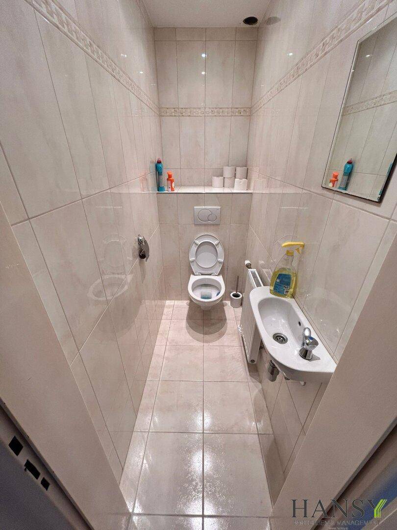 Kleines WC mit Toilette, Handwaschbecken und hellen Fliesen an Wänden und Boden.