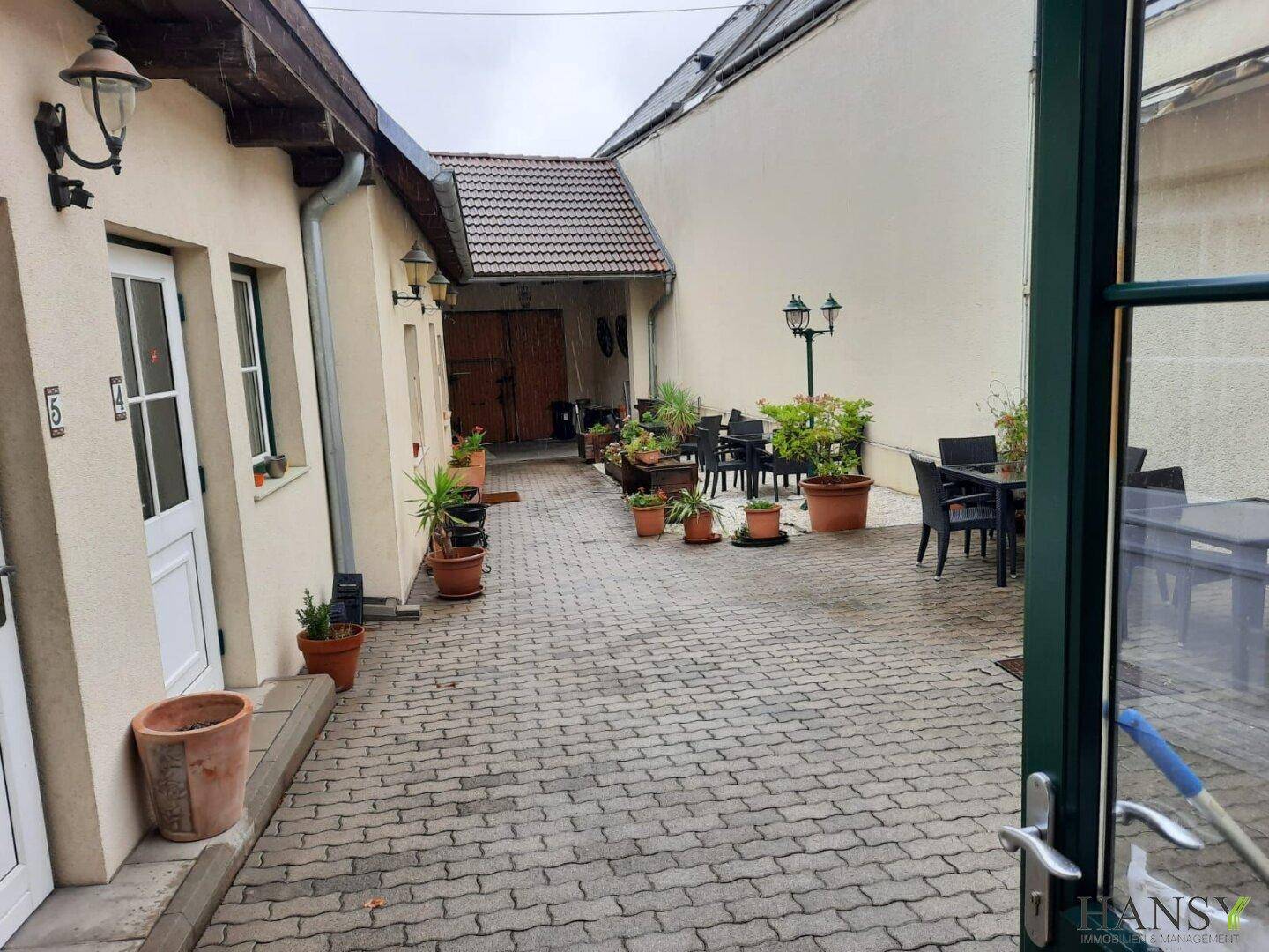 Gepflasterter Innenhof mit Sitzgelegenheiten im Freien und vielen Topfpflanzen, umgeben von Gebäuden.