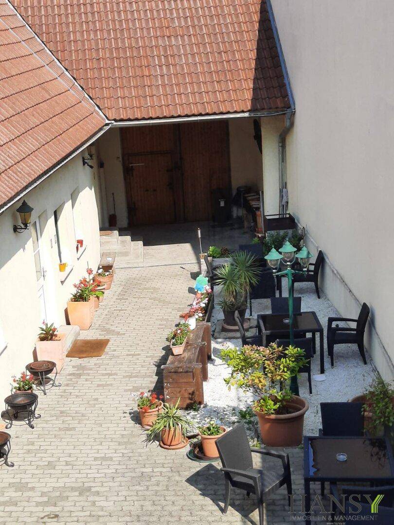 Blick von oben auf den gepflasterten Innenhof mit zahlreichen Pflanzen und gemütlichen Sitzgelegenheiten.