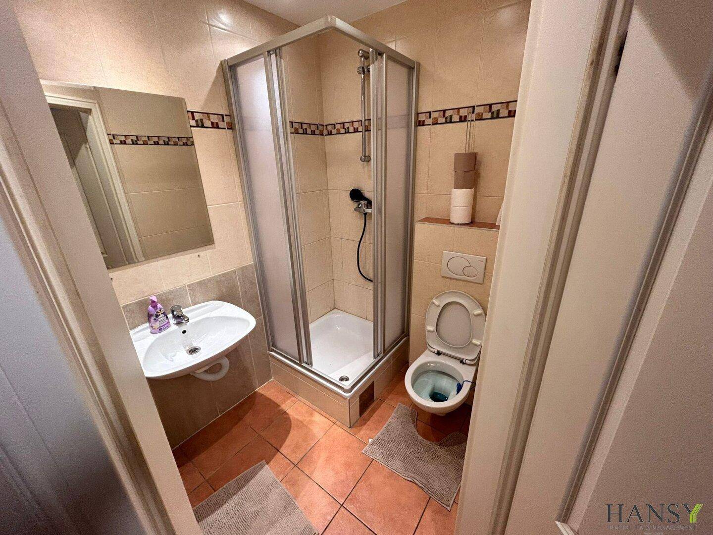 Badezimmer mit Duschkabine, Toilette und Waschbecken, ausgestattet mit beigen und braunen Fliesen.