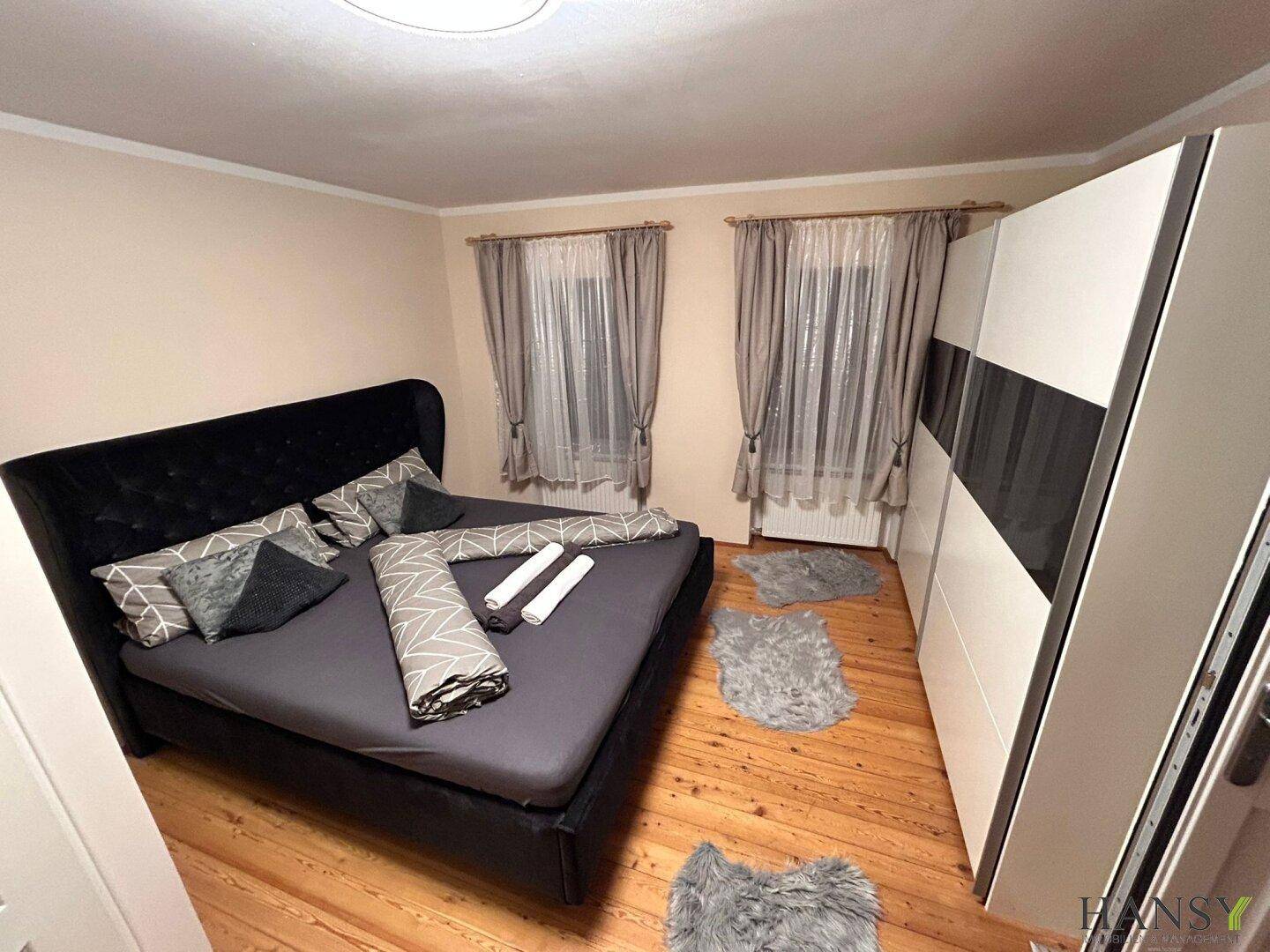Schlafzimmer mit dunklem Doppelbett, modernem Kleiderschrank und hellem Holzboden.