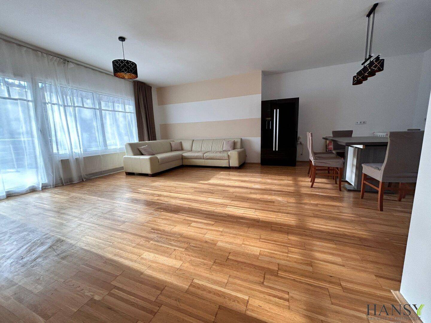 Großzügiger Wohn-Essbereich mit Holzboden, beigem Sofa und Esstisch, hell durch große Fenster.