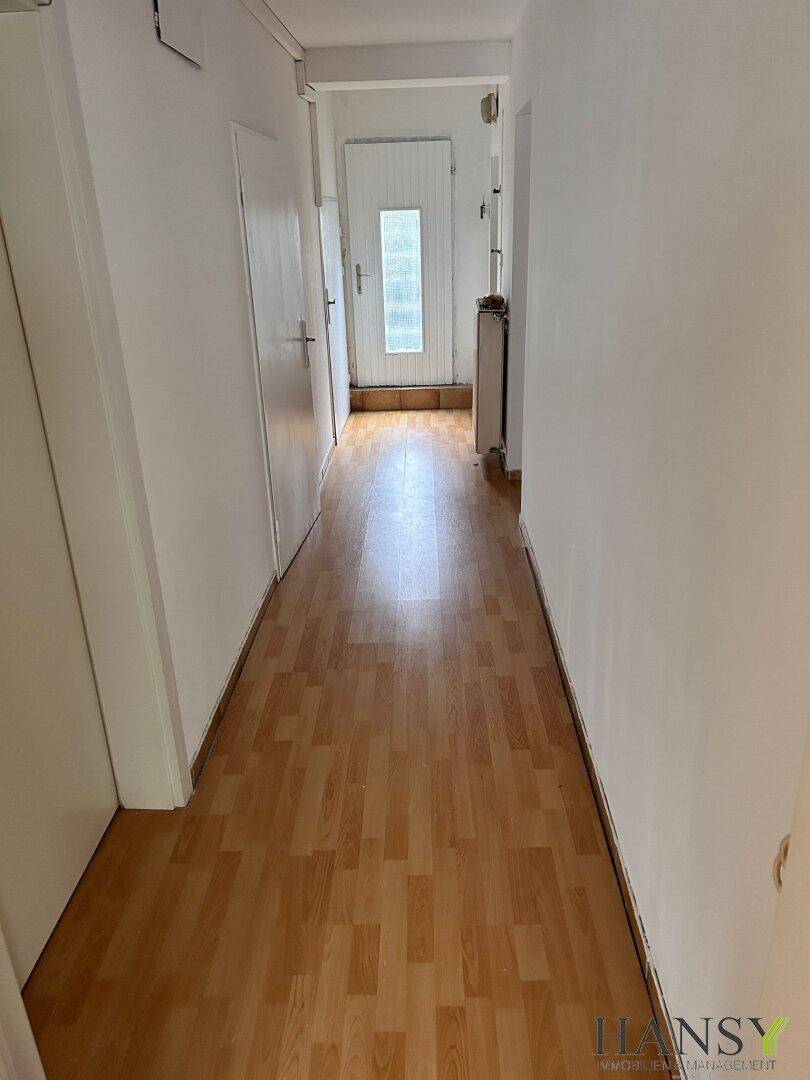 Langer, heller Flur mit Laminatboden und weißen Wänden, der zu weiteren Räumen führt.