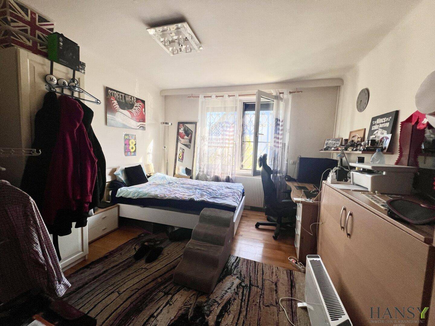 Helles Schlafzimmer mit Holzboden, großem Bett und Fenster zum Garten.