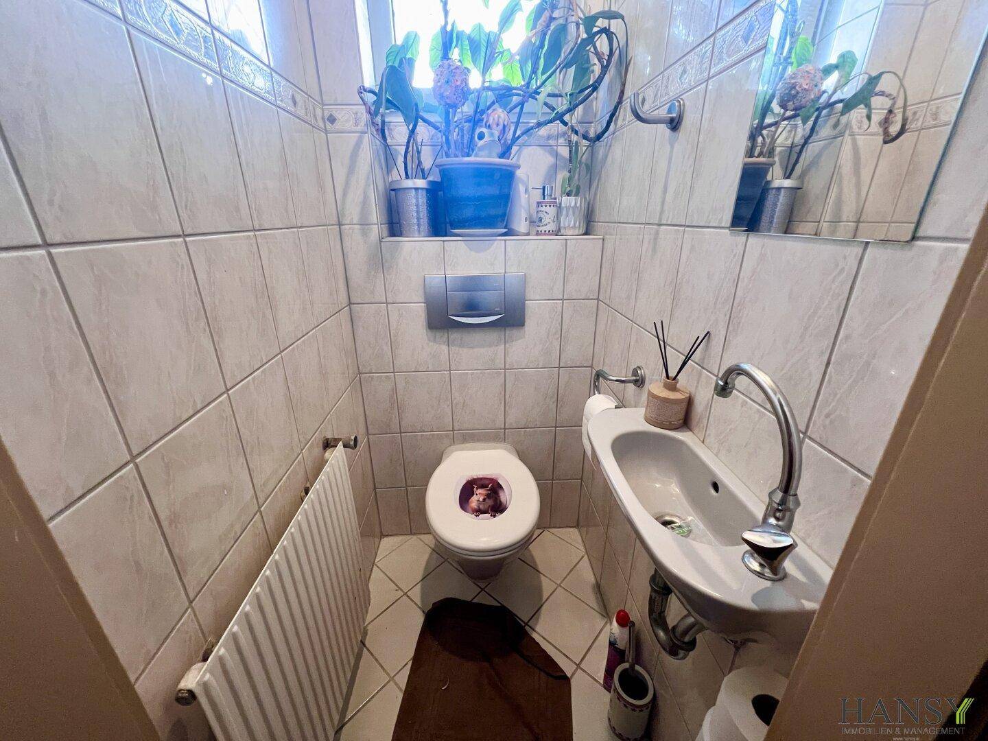 Kleines Gäste-WC mit Fliesen, Fenster und einem Waschbecken.