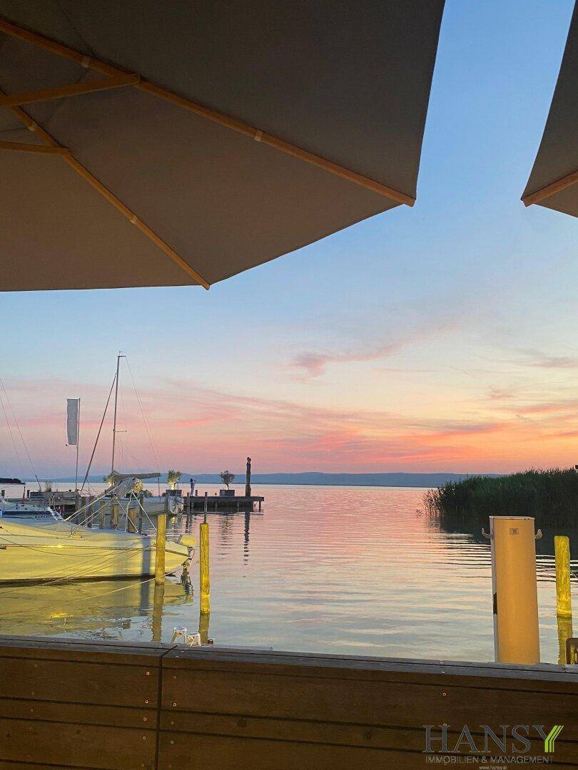 Malerischer Sonnenuntergang über einem See mit Booten und Schilf, gesehen von einem Steg.