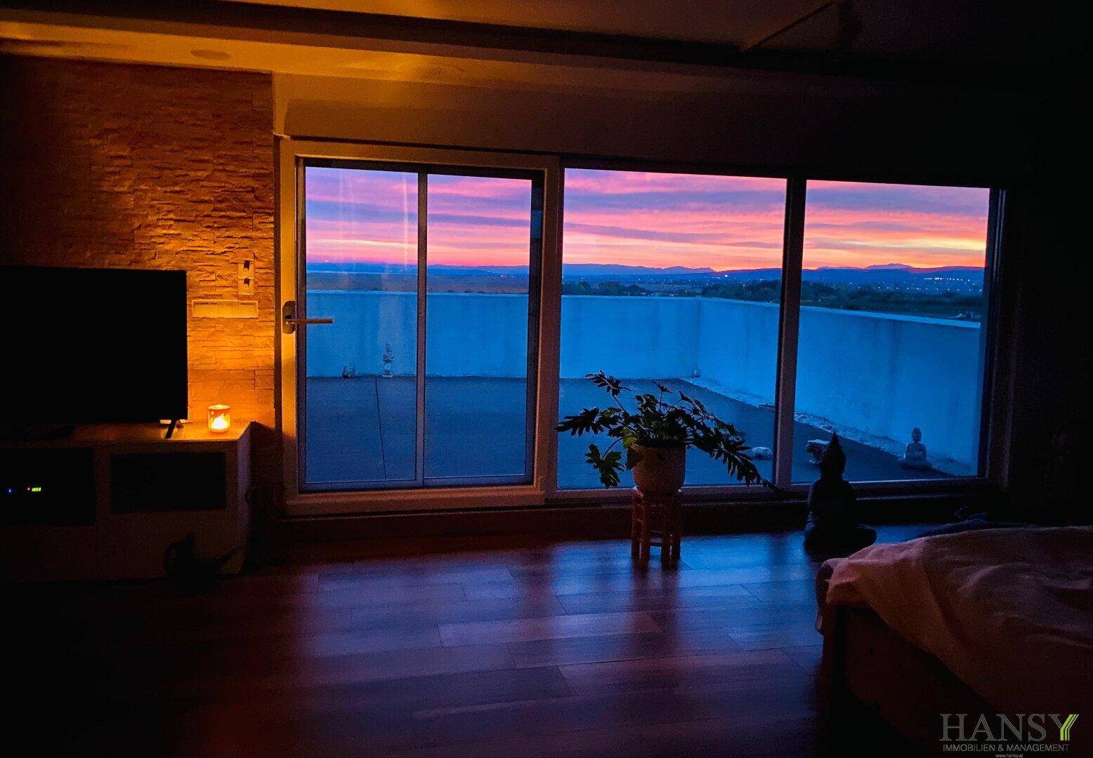 Schlafzimmer mit Blick auf den farbenprächtigen Sonnenuntergang über der weiten Landschaft.