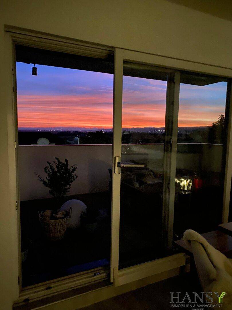 Spektakulärer Sonnenuntergang über der Landschaft, gesehen durch große Terrassentüren.