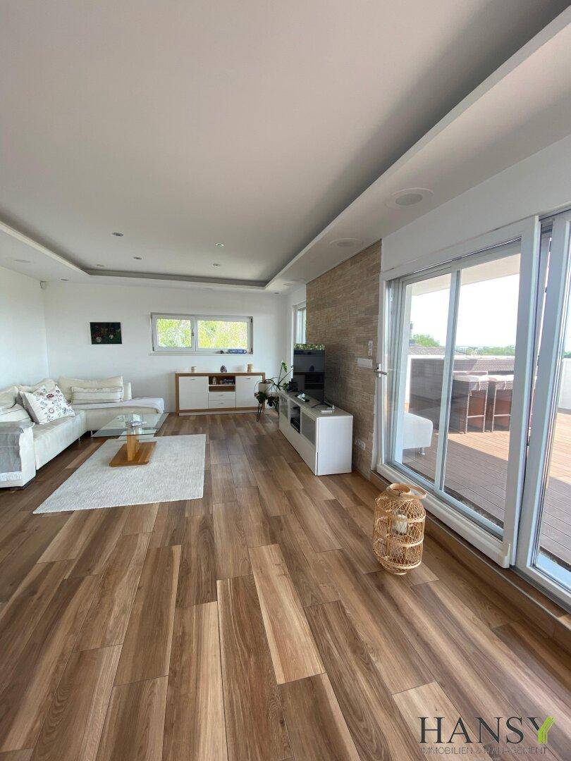 Geräumiges Wohnzimmer mit Holzoptik-Boden, bequemer Couch und Zugang zur Terrasse.