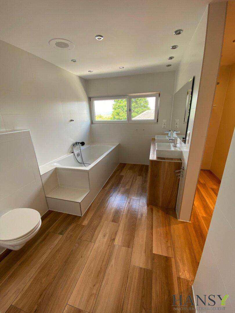 Modernes Badezimmer mit Badewanne, Doppelwaschbecken und Holzoptik-Fliesenboden.