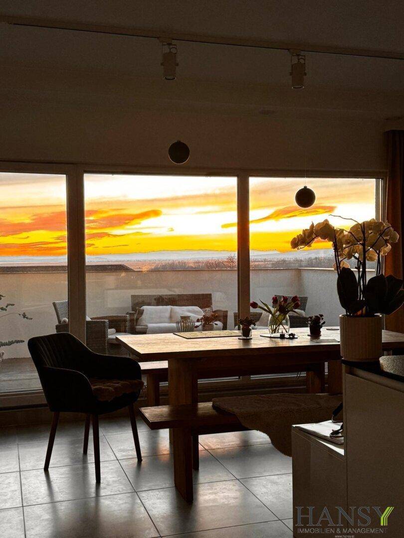 Essbereich mit Holztisch und Blick auf den spektakulären Sonnenuntergang von der Terrasse.