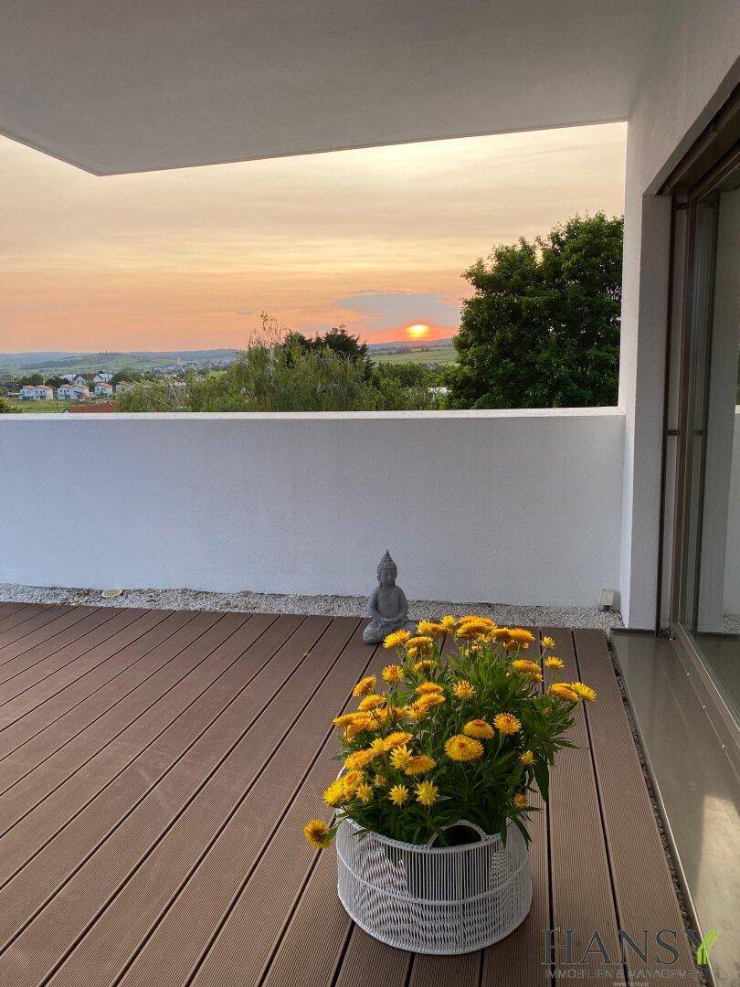 Sonnenuntergang über der Landschaft, genossen von einer Holzterrasse mit gelben Blumen.