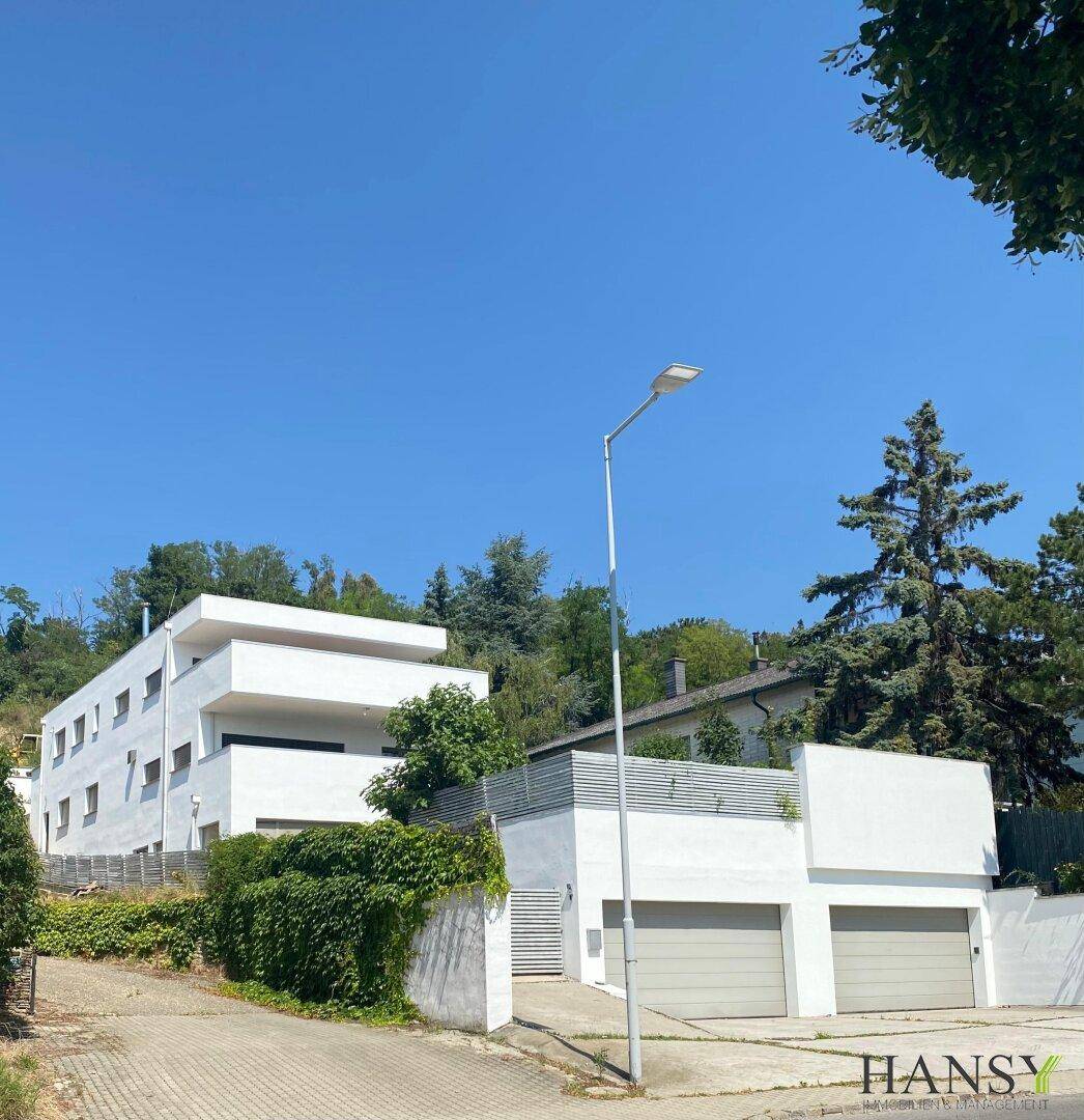 Moderne Wohnanlage mit weißer Fassade, Garagen und üppiger grüner Bepflanzung.