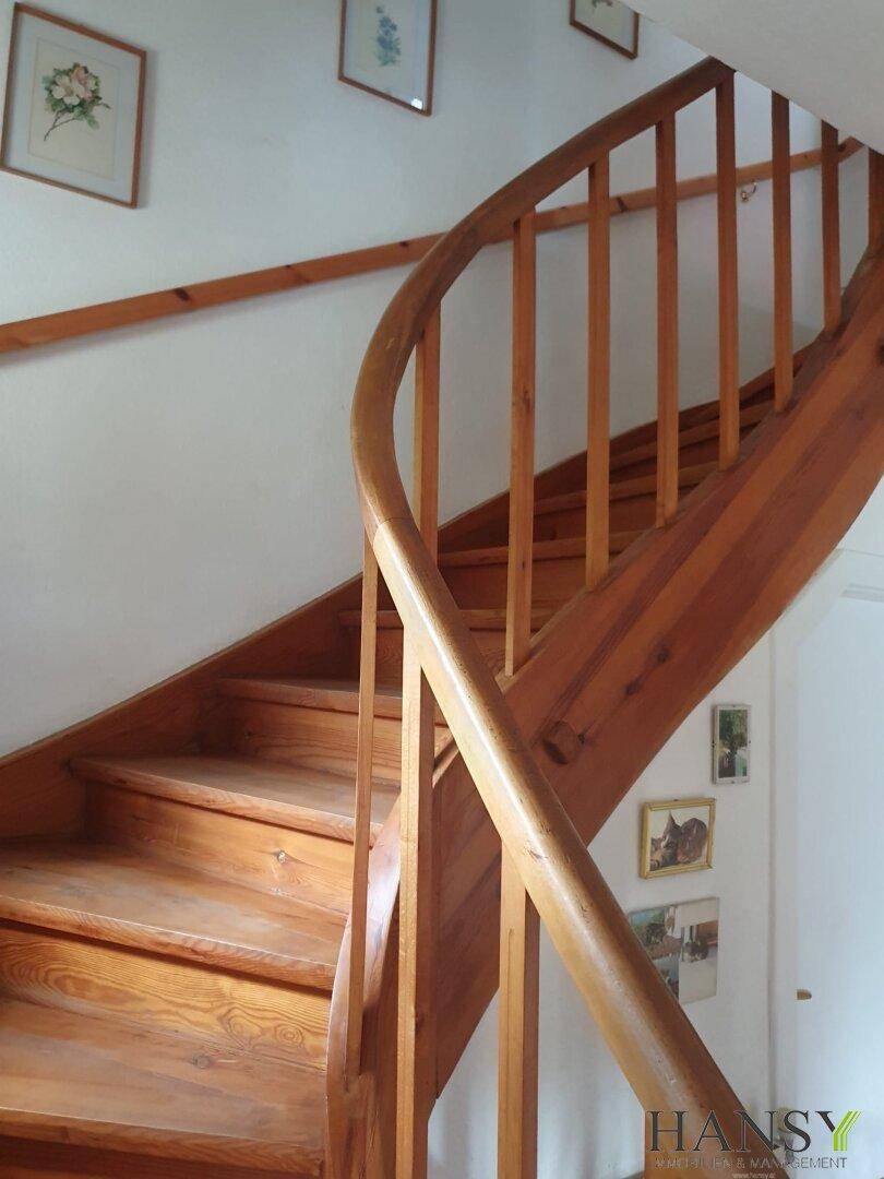 Geschwungene Holztreppe mit einfachem Geländer, die die verschiedenen Etagen des Hauses verbindet.